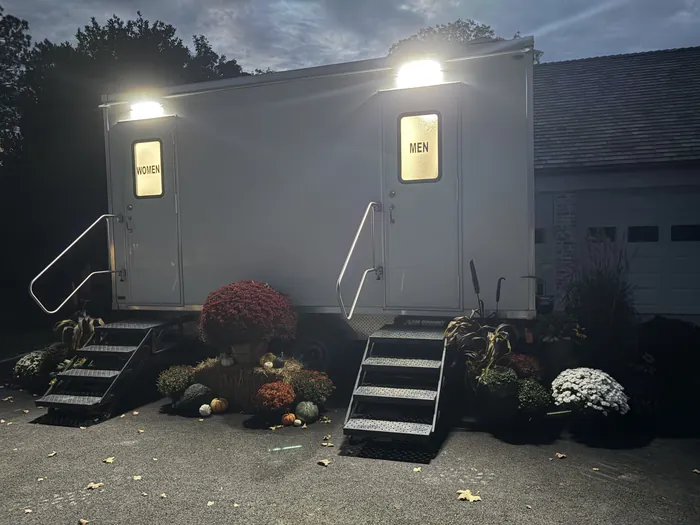 Clean Spot two station restroom trailer lit up at dusk with fall mums, pumpkins and hay bales around the steps